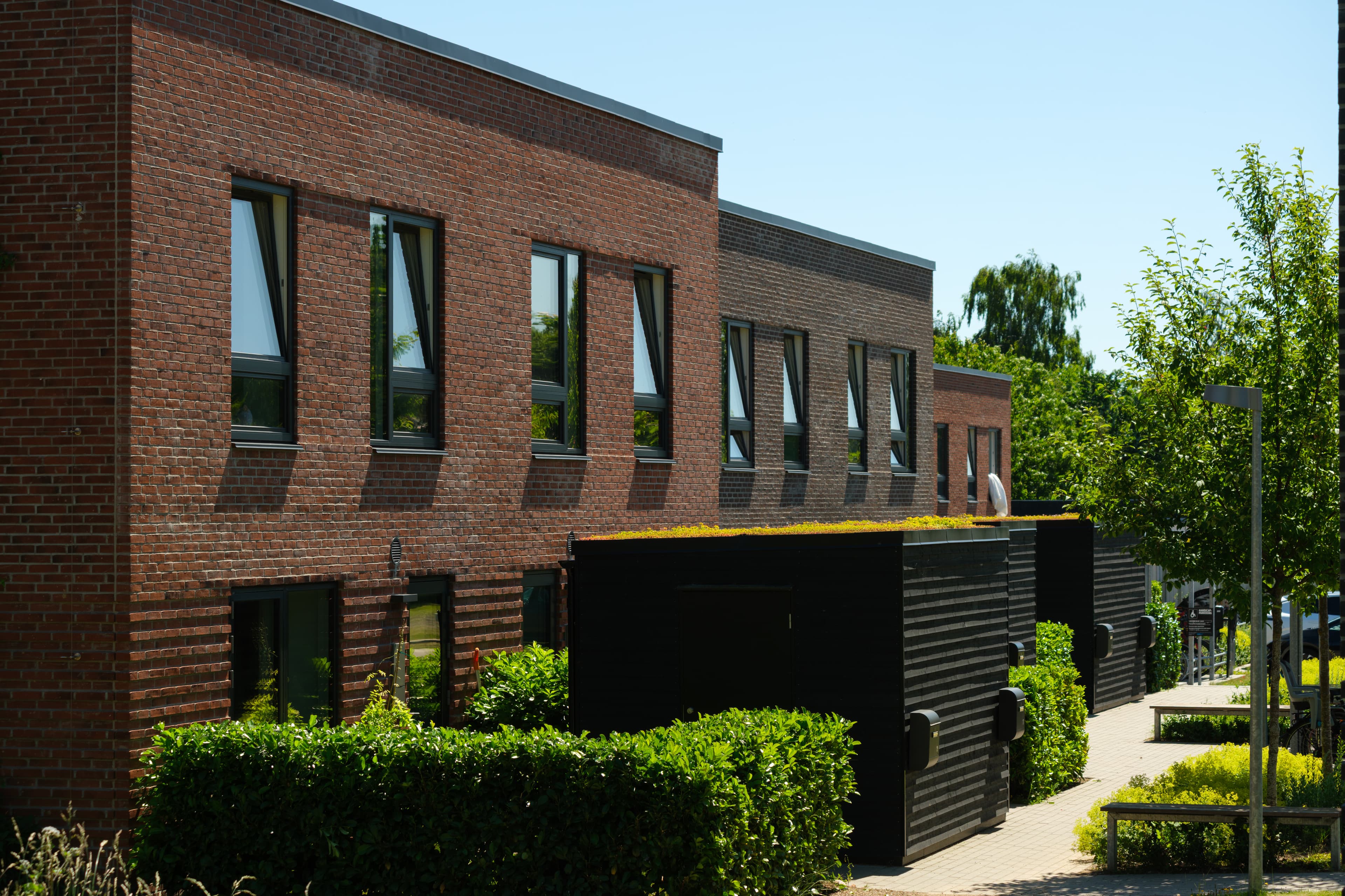 This photo shows the façade and the associated storragde and bike shed for the TriumphHusene terraced houses in Espergærde.