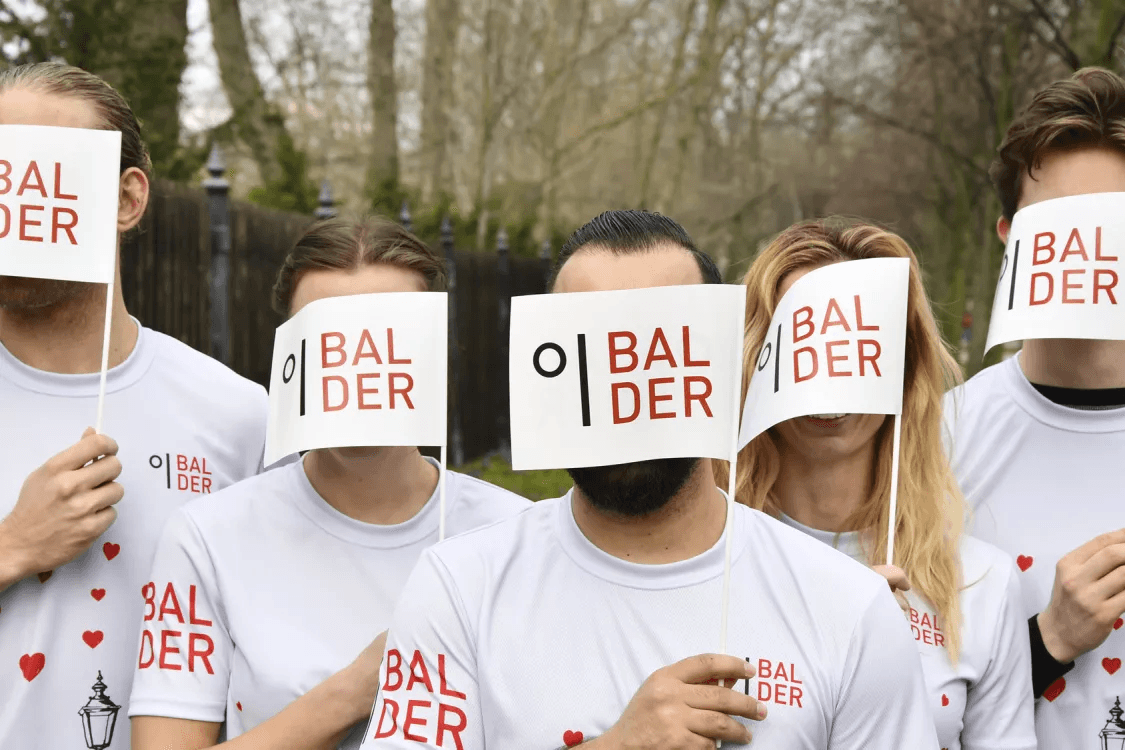 Balder employees hold a Balder flag in front of their faces.