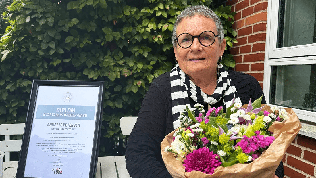 Annette stands on her terrace at Østerfælled Torv with flowers and a certificate