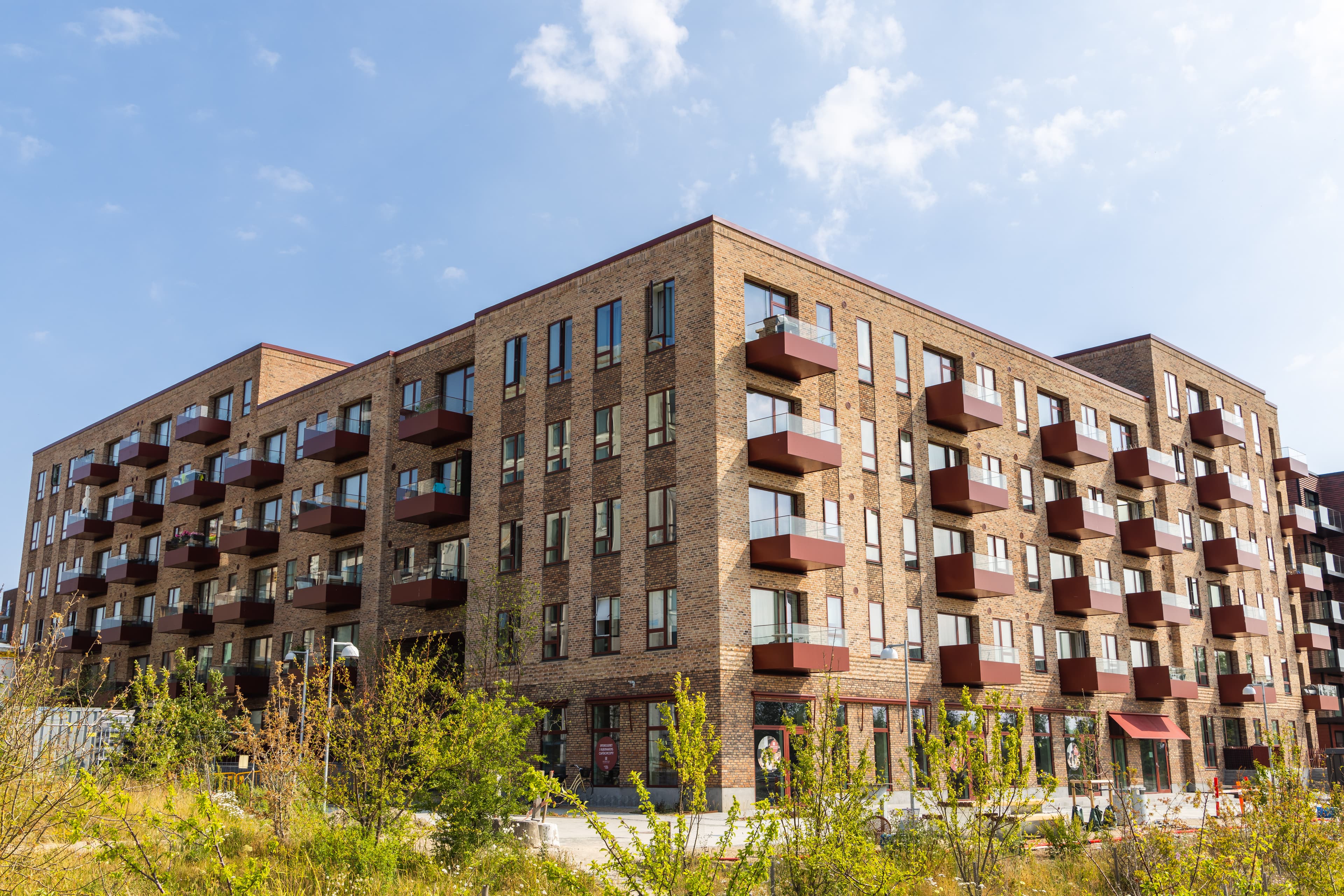 Image showing the red balconies and brick façade of the square building constructed across multiple levels at the property Rubinhaven in Høje-Taastrup.